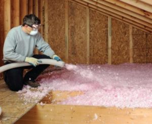 Man installing fiberglass insulation in attic