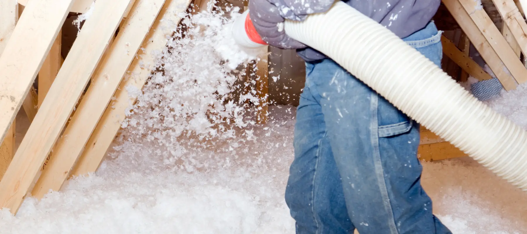 worker spraying blown fiberglass insulation between attic trusses
